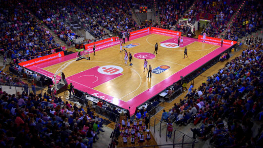 Basketball arena with a pink court, seen from the stands