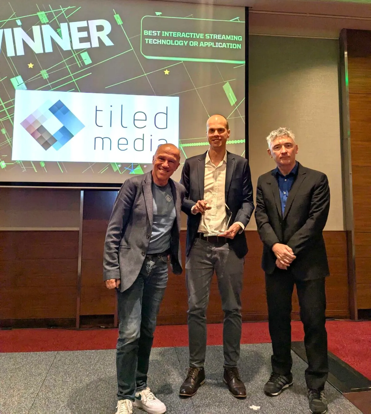 Three Tiledmedia colleagues on stage with the CSI award, winner slide behind them