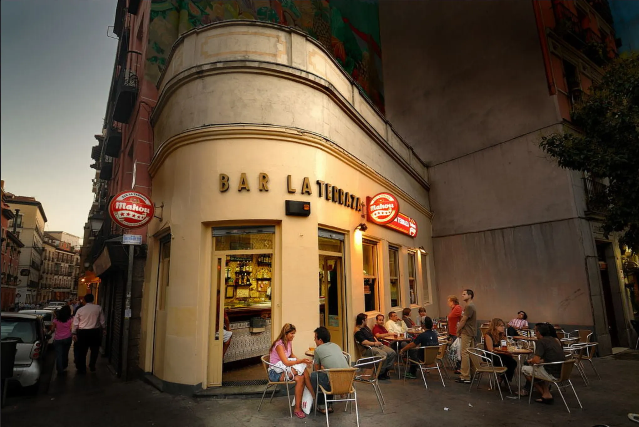People sitting at outdoor tables in front of a street corner bar