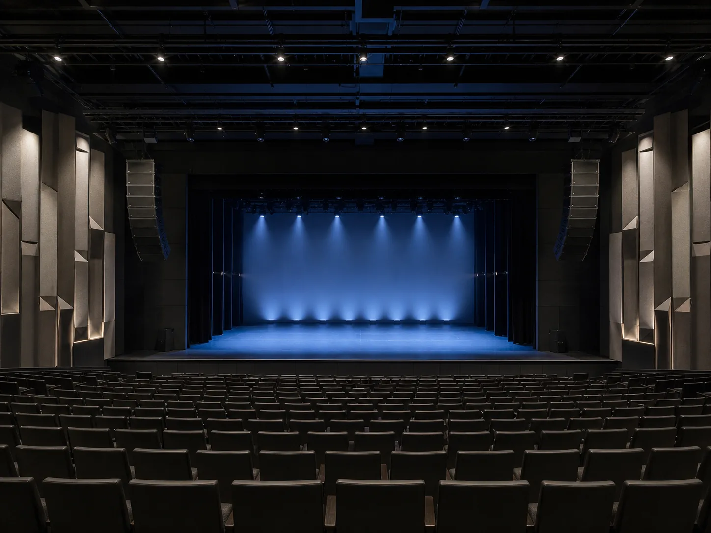 Conceptual empty auditorium with stage lighting, acoustic treatment, seating, and large-format sound system