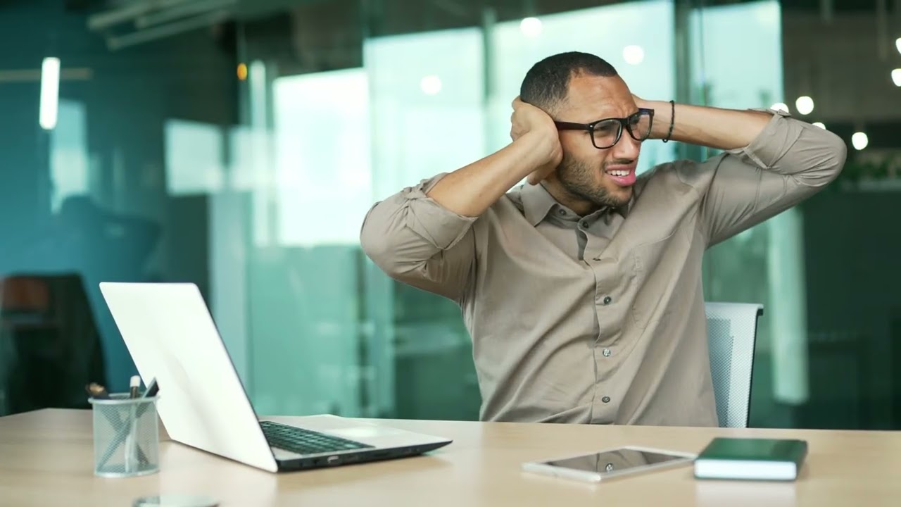 Frustrated participant covering his ears beside a laptop in a conference room.