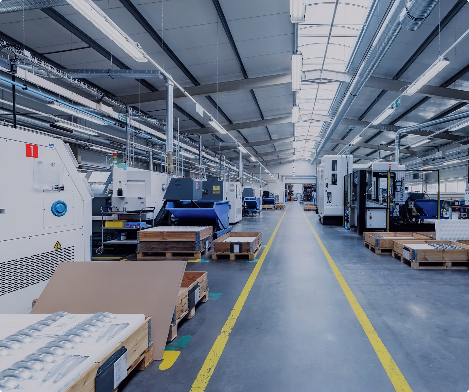 Moderne Fabrikhalle mit industriellen Maschinen, Paletten und gelben Bodenmarkierungen.