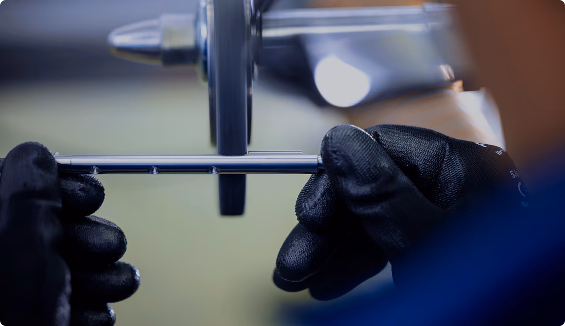 Person mit schwarzen Handschuhen hält ein Metallstück vor einem rotierenden Schleifwerkzeug.