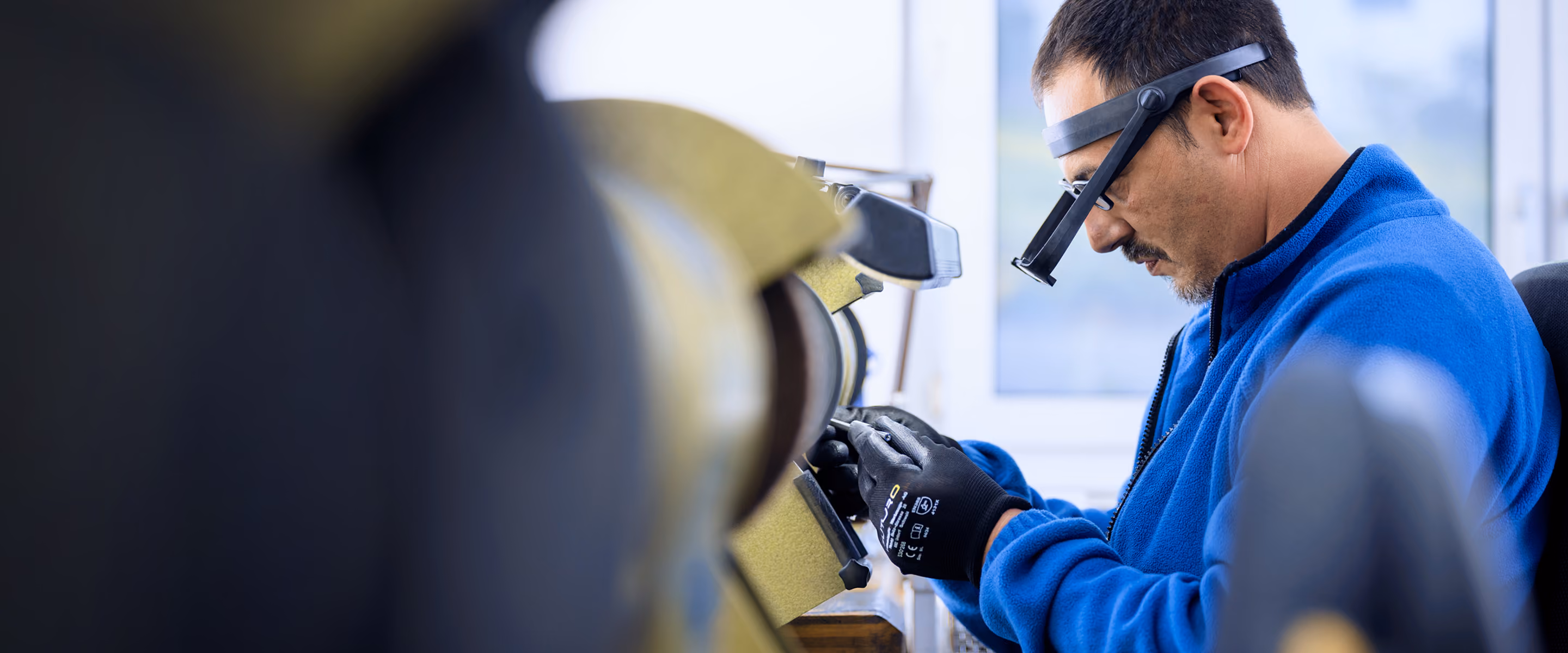Mann in blauer Jacke mit Vergrösserungsglas arbeitet konzentriert an einer Maschine.