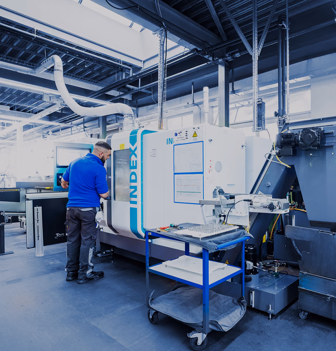 Mann neben einer Index CNC-Maschine in einem modernen, gut beleuchteten Industriegebäude.