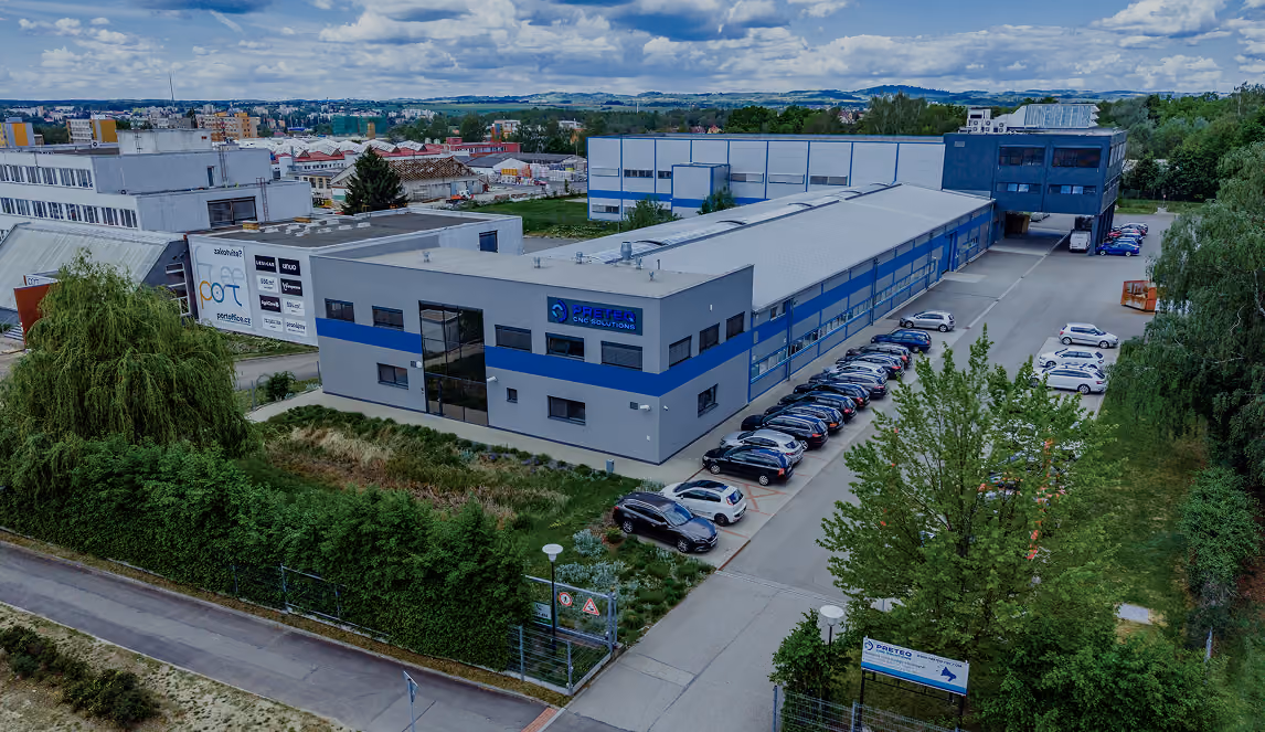 Luftaufnahme eines modernen Industriegebäudes mit Parkplätzen und umliegendem Grün.
