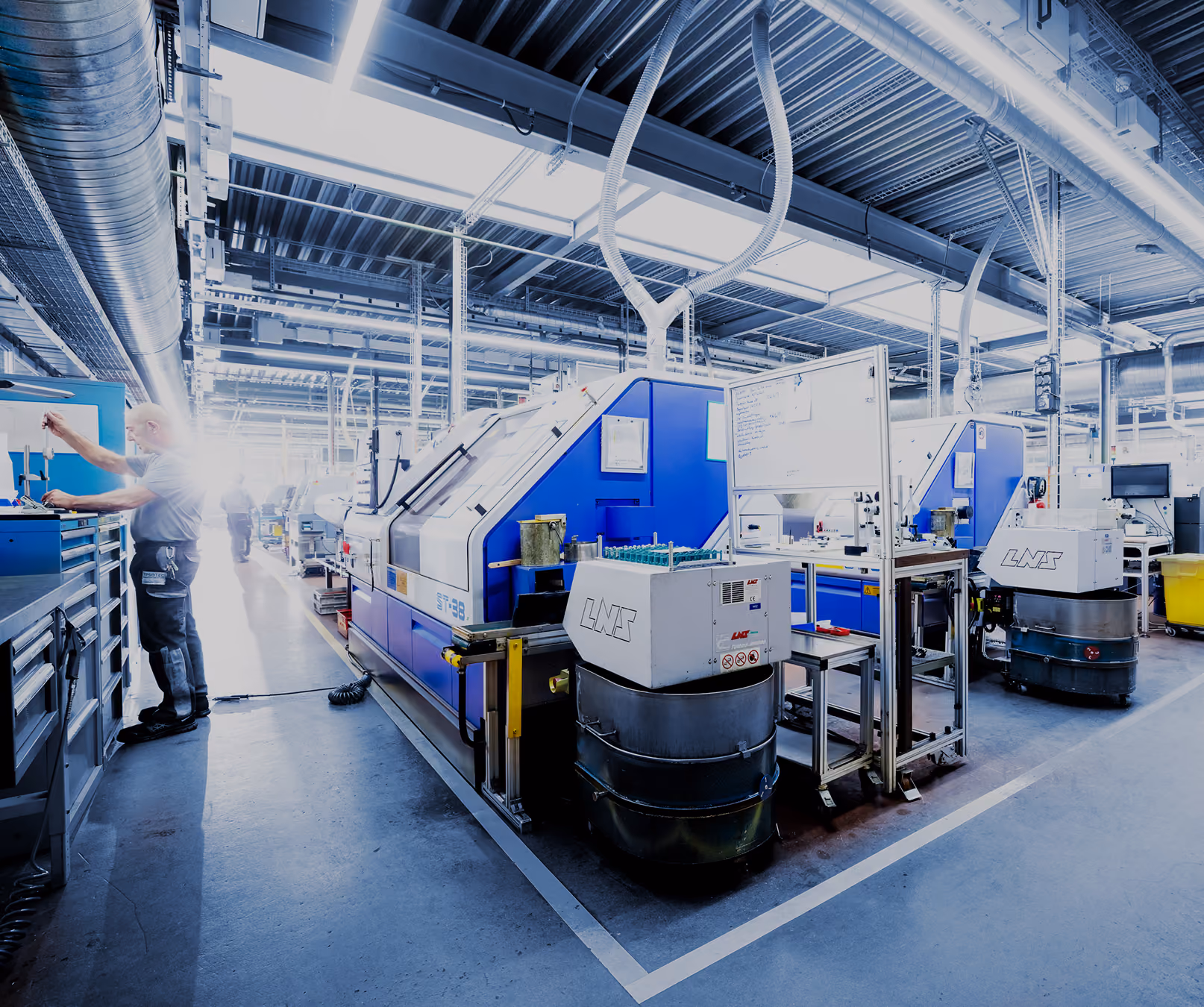 Mitarbeiter arbeitet an Werkzeugschrank neben blauen Industrieanlagen in einer hell beleuchteten Fabrik.