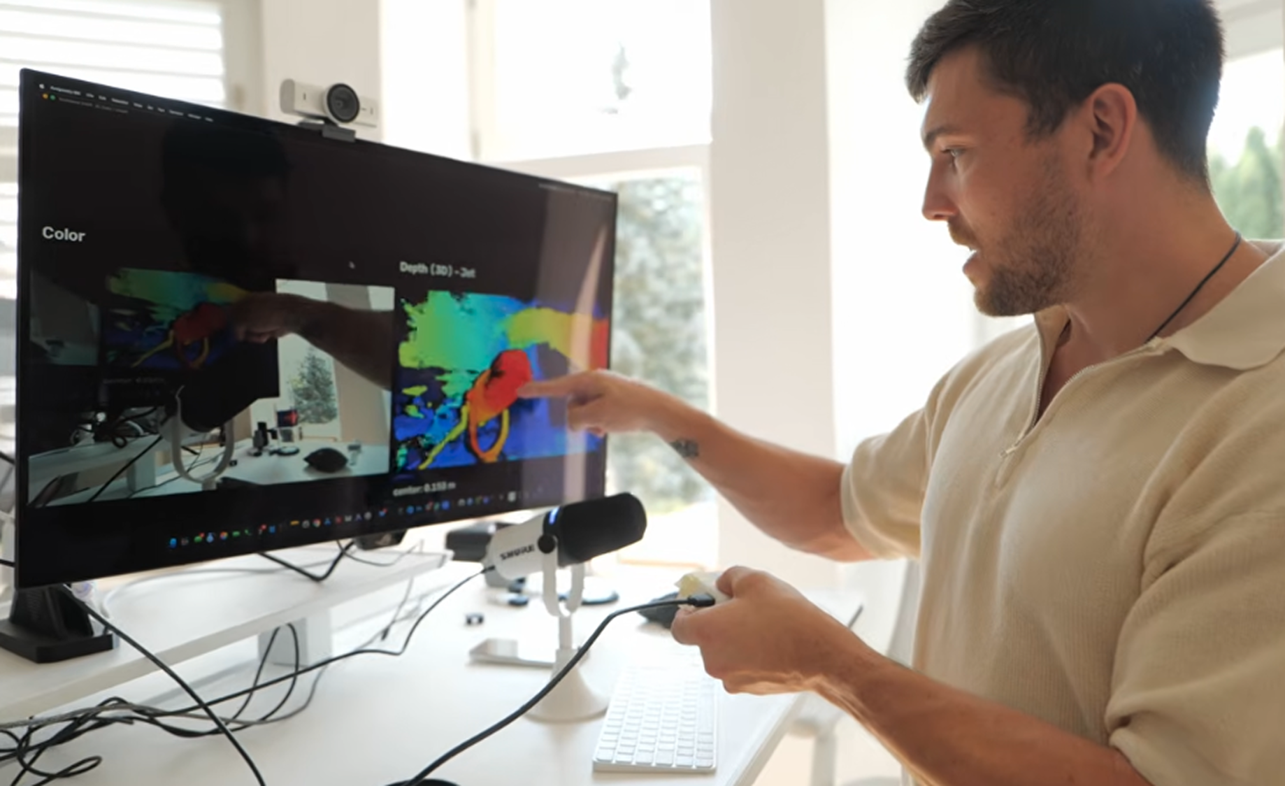 Man pointing at color-coded depth data on a computer screen in a bright room, holding a device.
