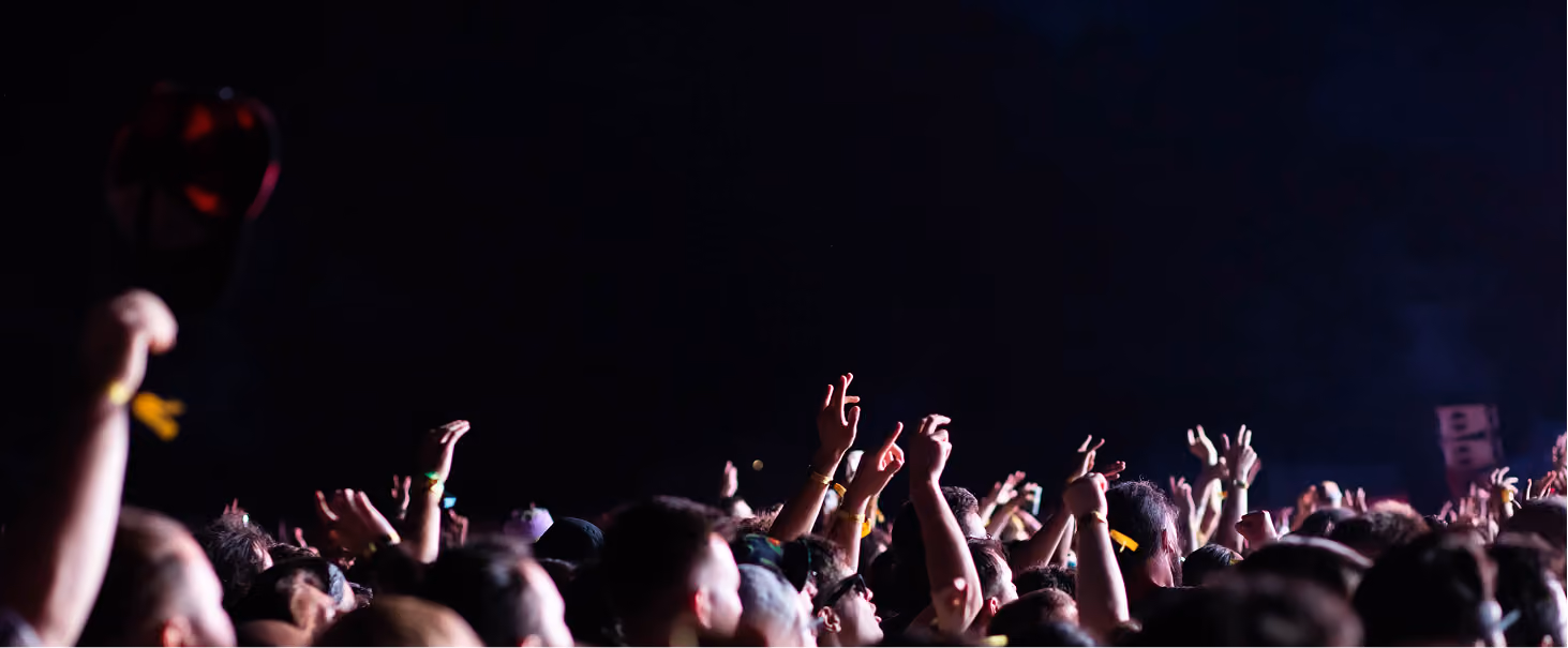 Crowd of people at night with raised hands, some making peace signs or pointing upwards against a dark sky.