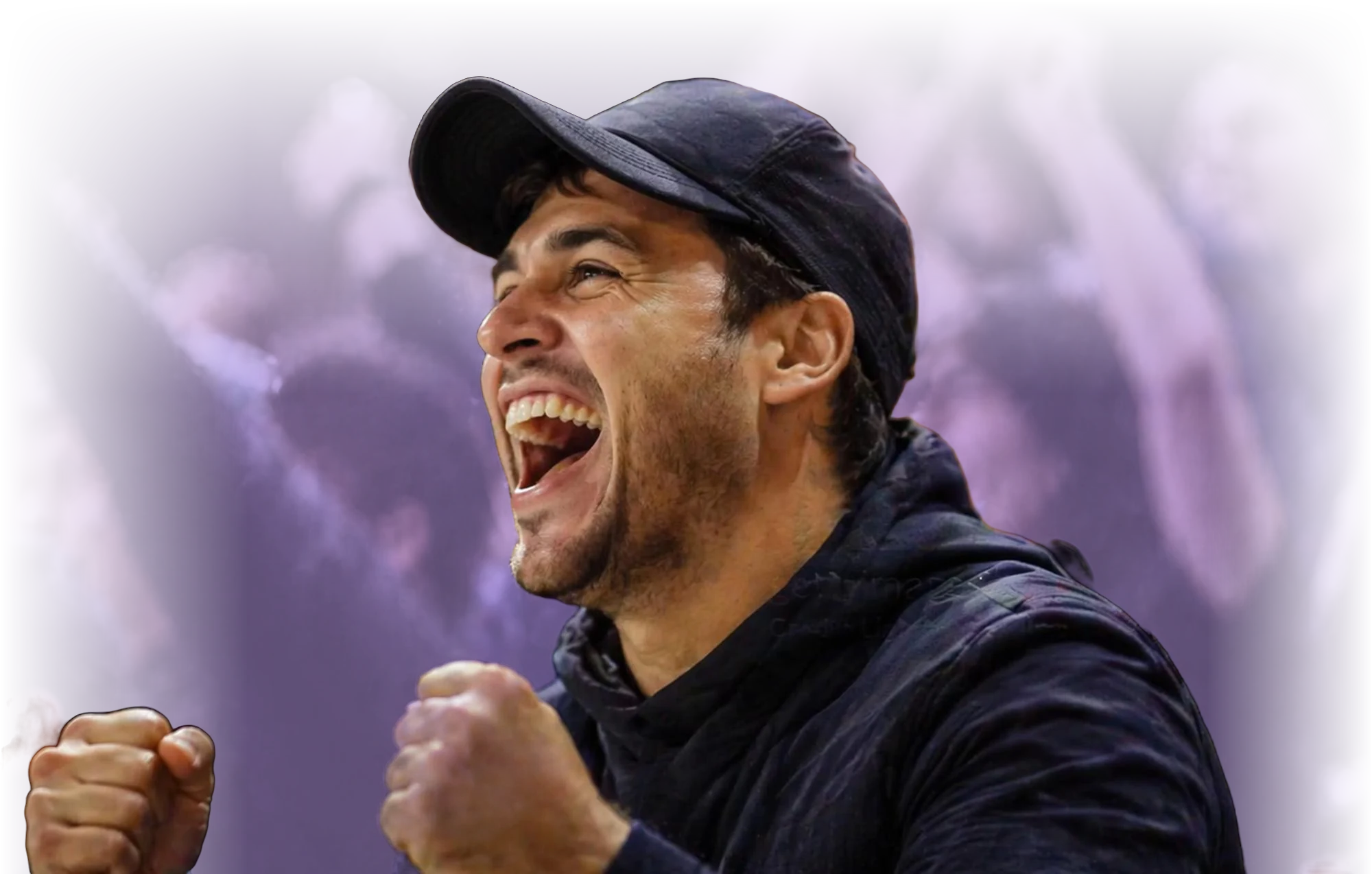 Close-up of a man wearing a black cap and jacket, cheering enthusiastically with fists clenched and mouth open, with a blurred crowd in the purple-toned background.