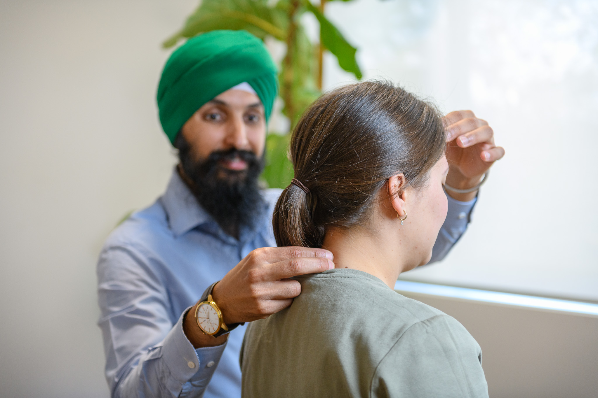 A man wearing a green turban and light blue shirt gently touches the back of a woman's neck who has brown hair tied in a ponytail.