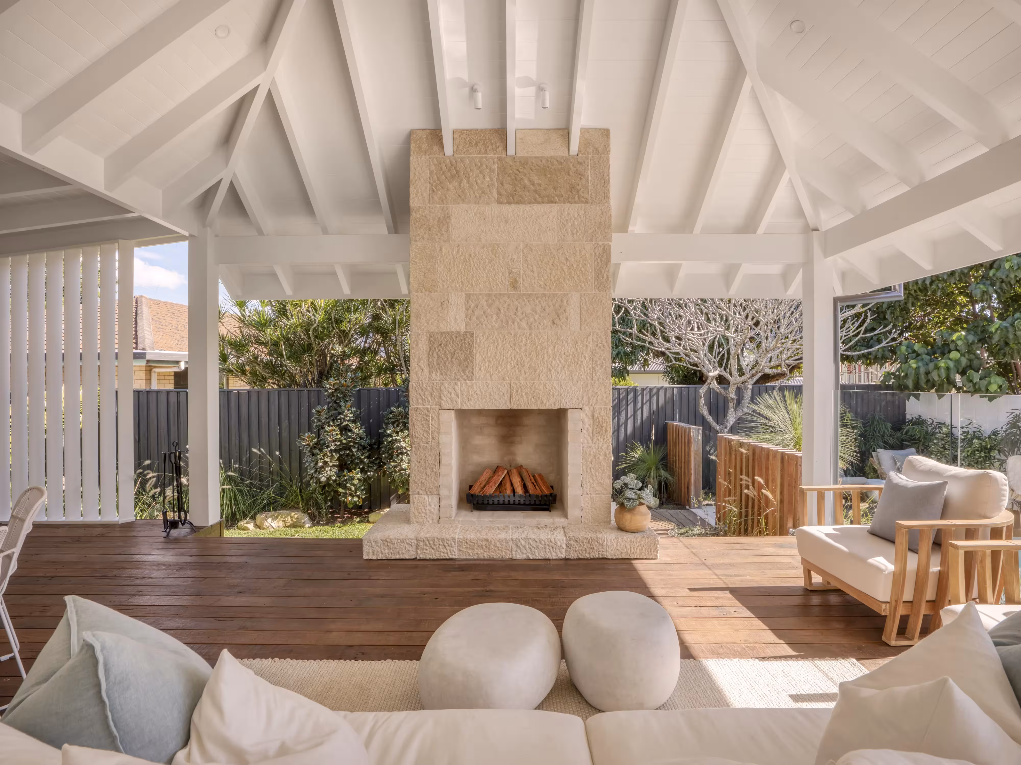 Covered outdoor living area with a central stone fireplace at Aruma Avenue.