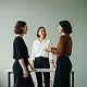 Three women in business attire standing and talking in a professional office setting.