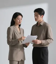 Two professionally dressed people discussing and holding documents in a neutral setting.