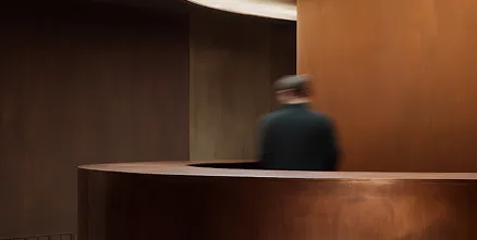 Person standing behind a curved copper-toned modern reception desk in a dimly lit room.