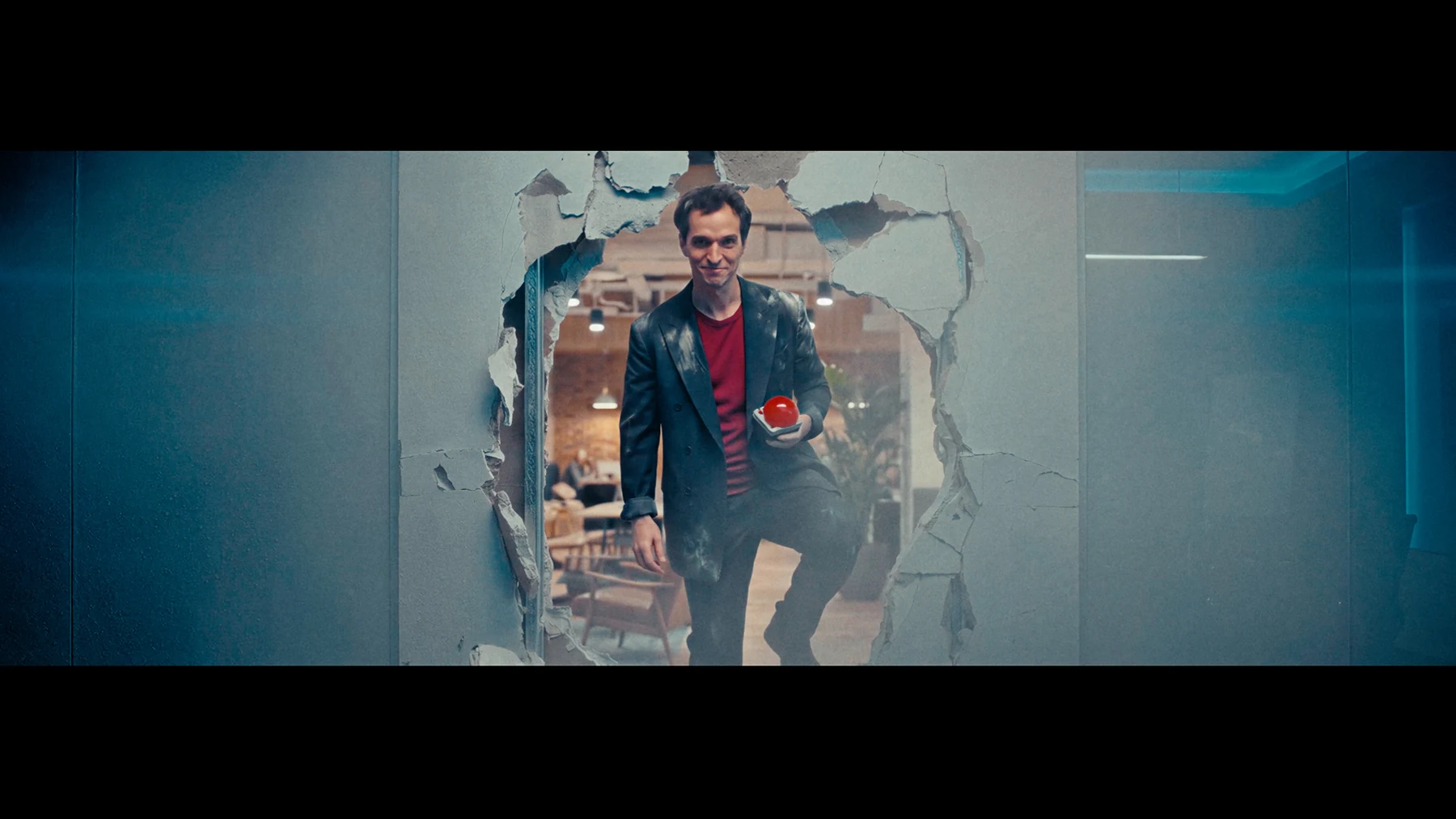 Indispensable — A man steps through a broken studio wall holding a red button