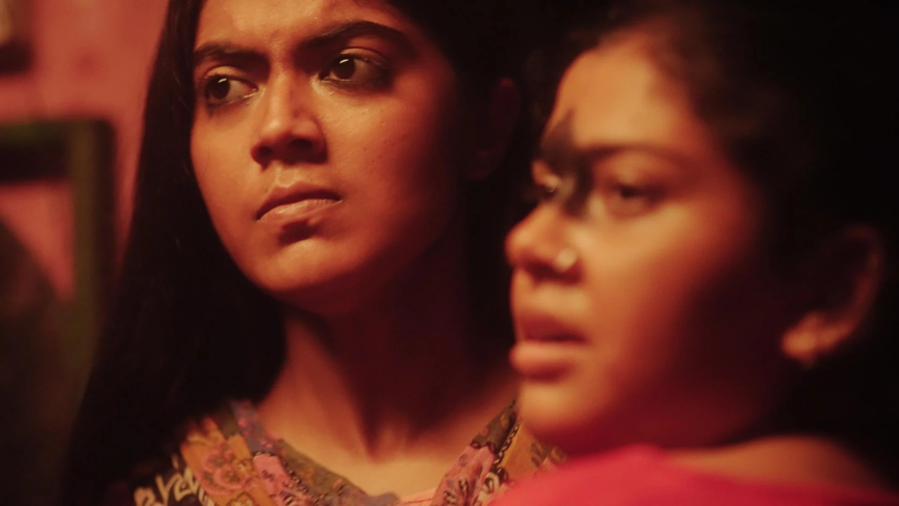 Kali — Two women share an intense glance in red light