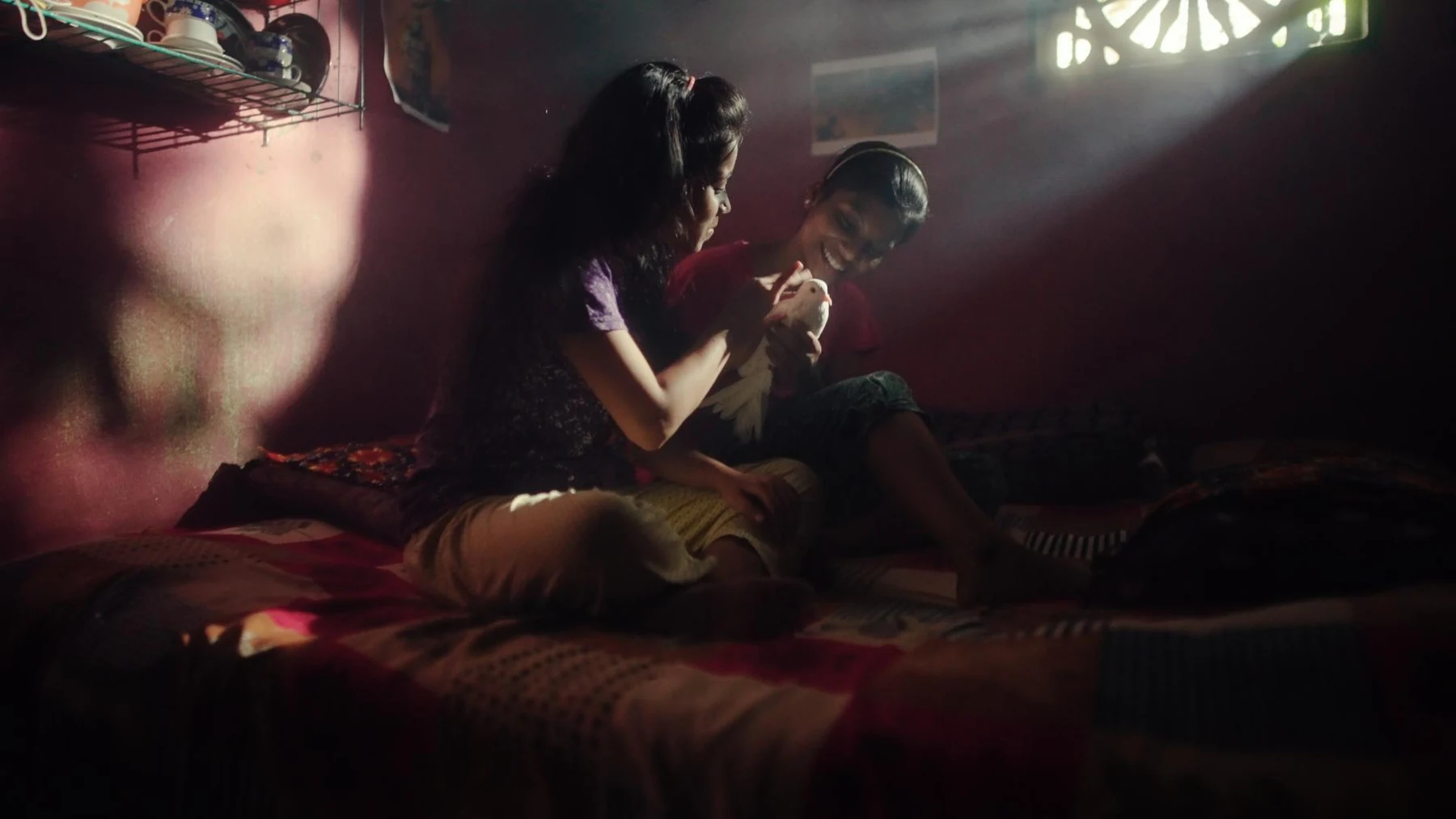 Kali — A quiet family moment in a red room crossed by sunlight