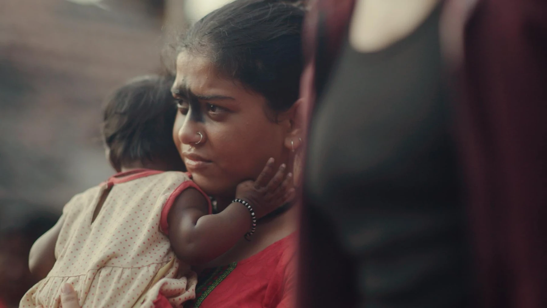 Kali — A woman holds a child close and watches anxiously