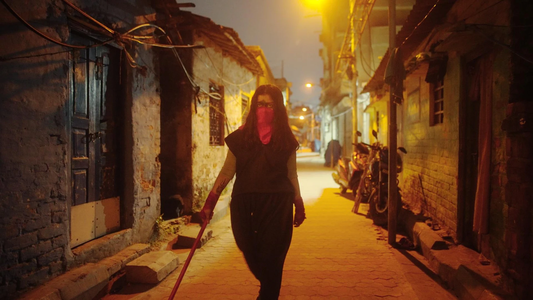 Kali — A masked vigilante walks through an amber-lit Kolkata lane
