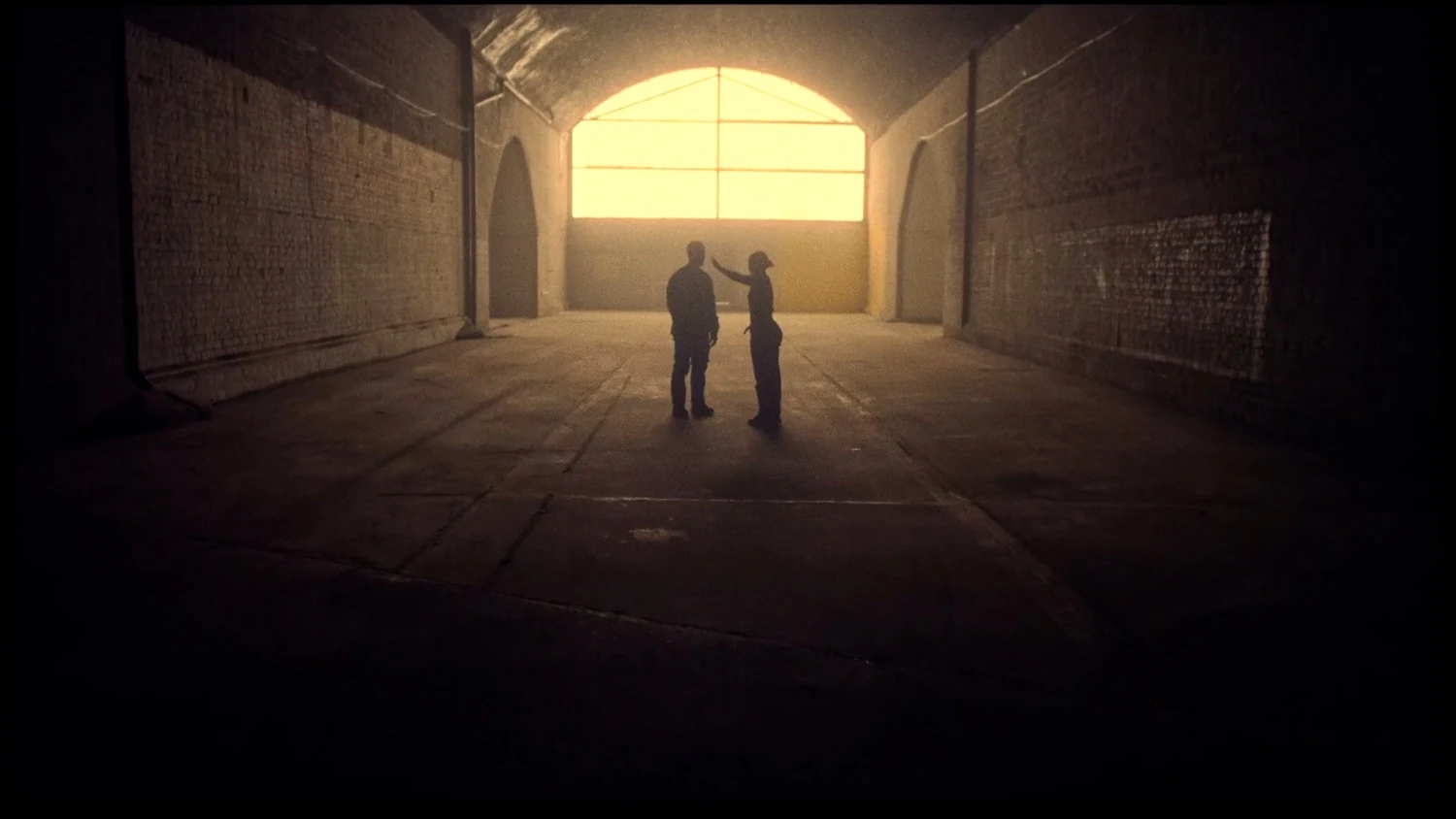 Movement — two silhouettes in an empty warehouse, backlit by a glowing arched window