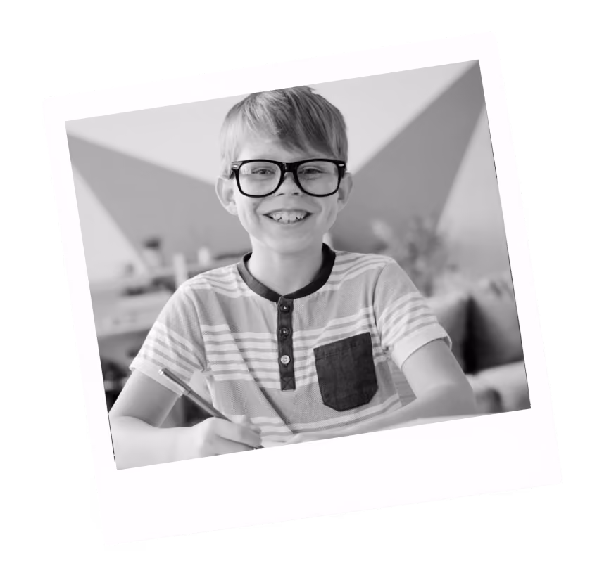 Smiling boy with glasses writing with a pencil, wearing a striped shirt with a pocket.