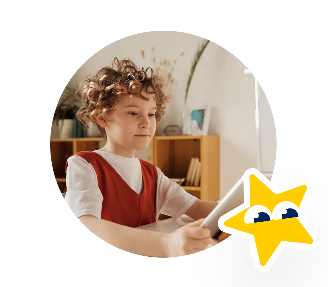 A young child with curly hair wearing a red sleeveless dress over a white shirt, holding and looking at a tablet in a cozy room with a wooden bookshelf and plants in the background.