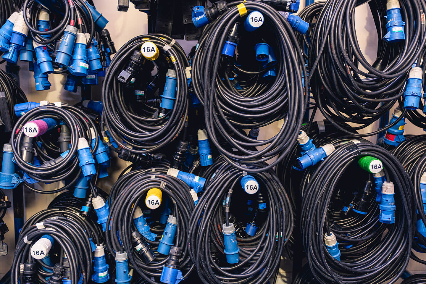 Multiple coiled black power cables with blue connectors hanging on a wall.