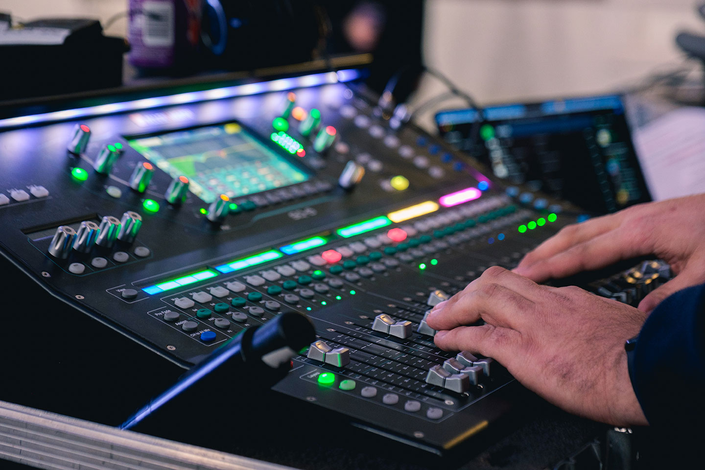 Hands adjusting sliders on a professional sound mixing console.