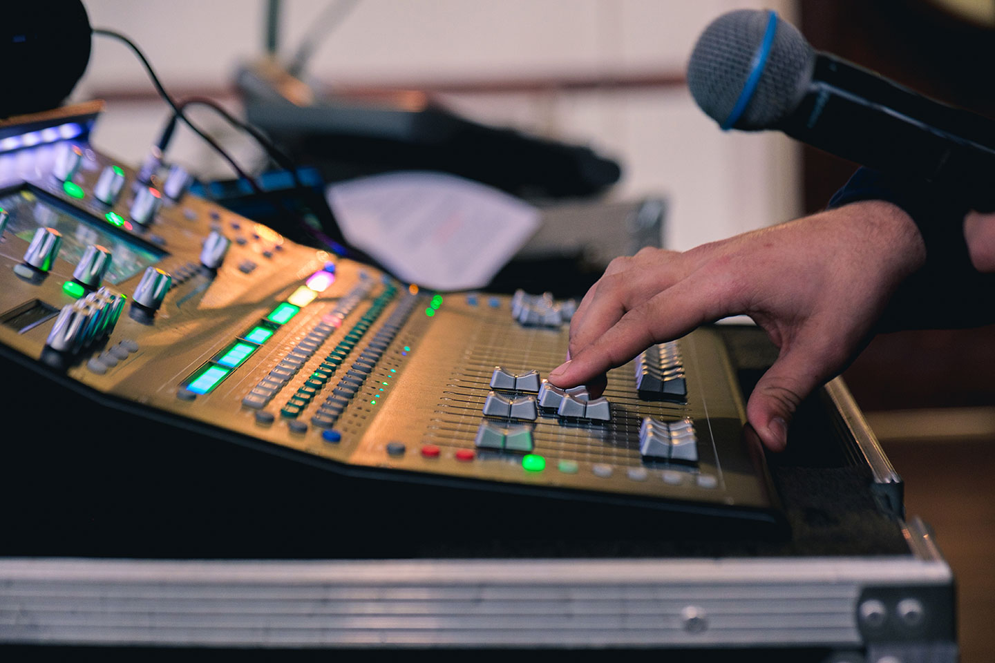 Person adjusting sliders on a professional audio mixing console with a microphone in hand.