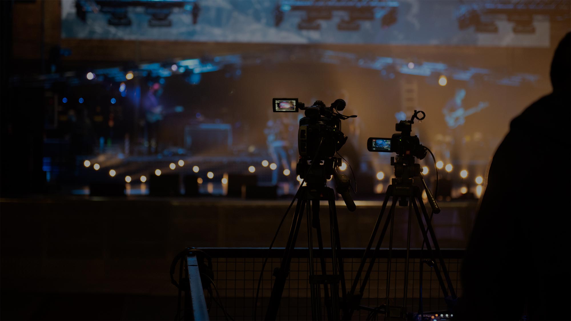 Two video cameras on tripods recording a stage with musicians playing live