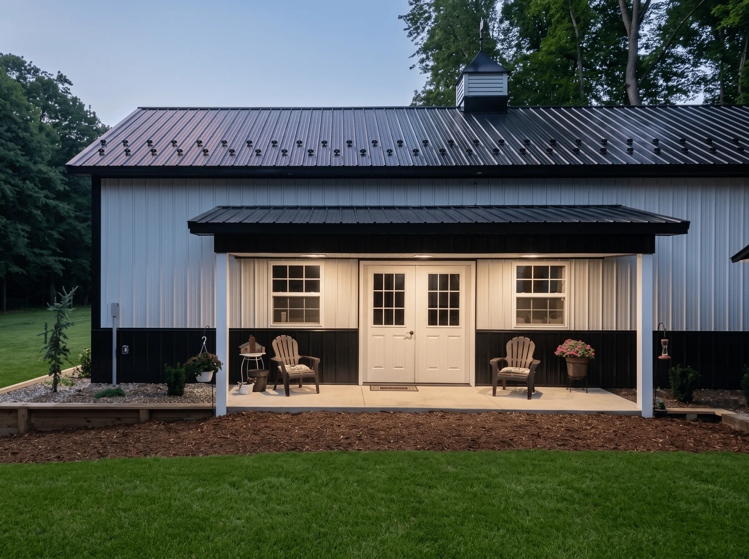 A modern black and white barn with double doors, a small covered porch, two Adirondack chairs.
