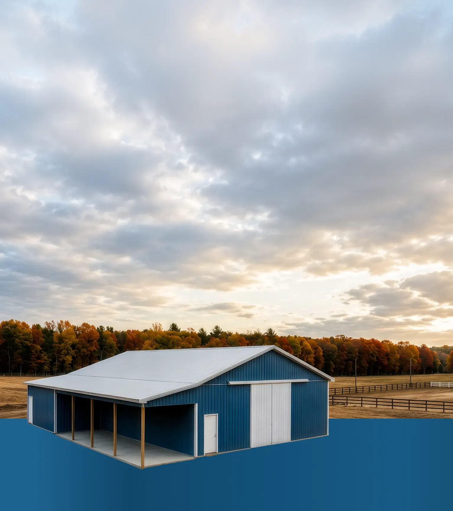 A blue barn stands in front of autumn trees and fenced fields under a cloudy sky.