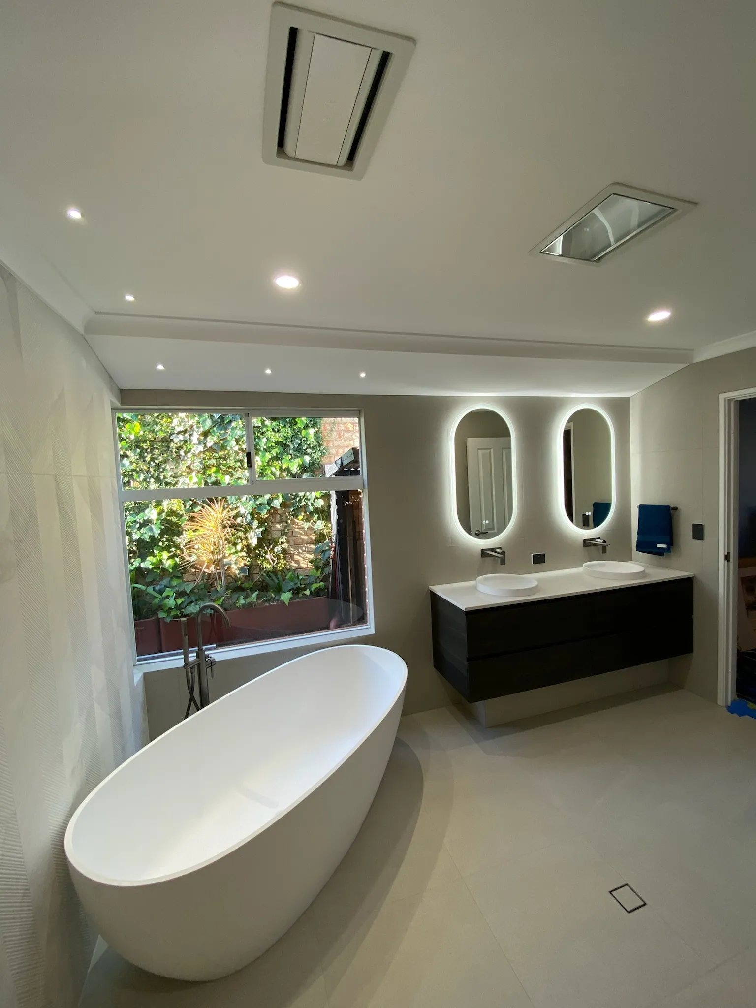 Bathroom with downlights above a freestanding bath and twin round mirrors