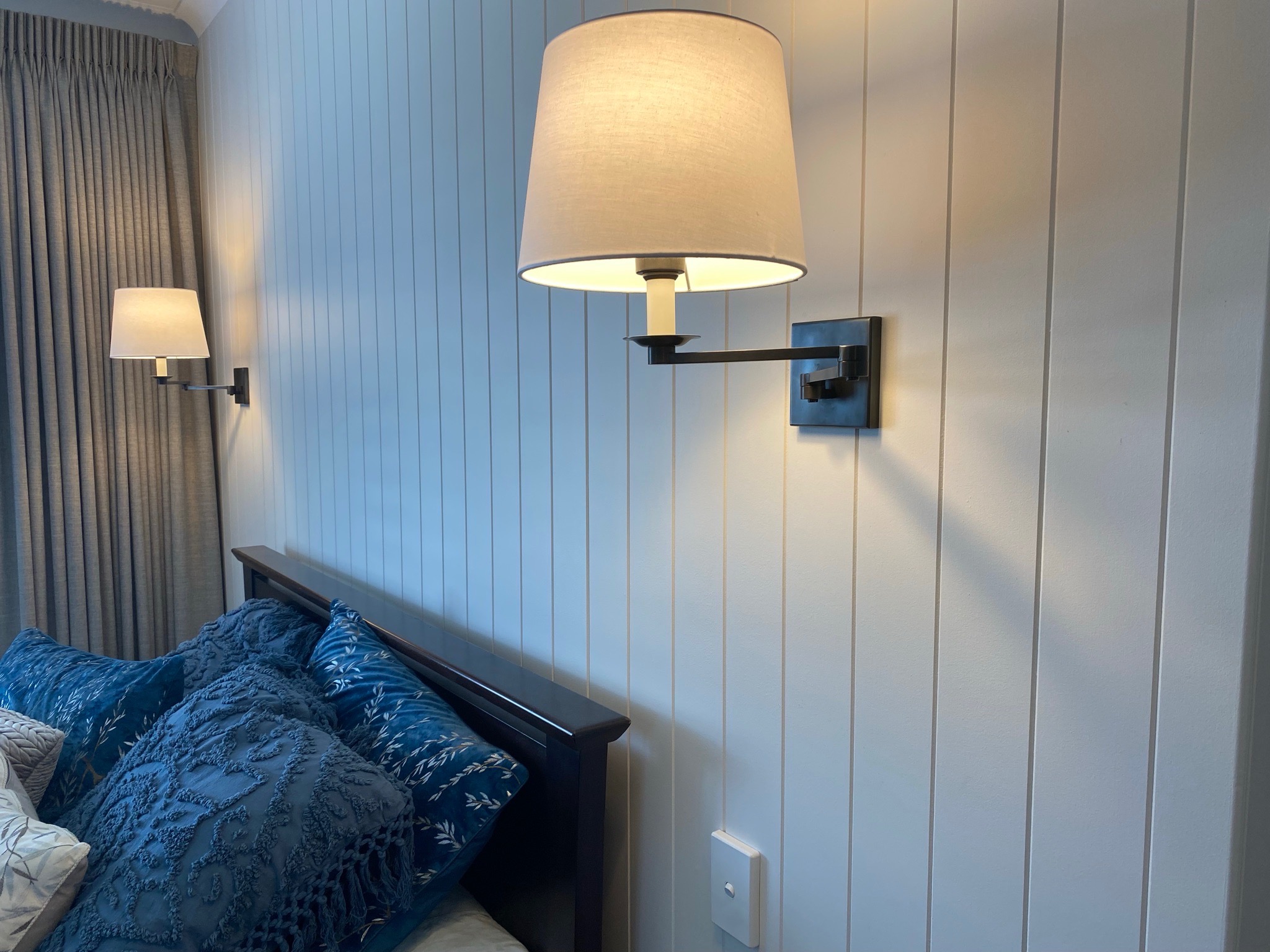 Wall mounted bedside lights installed on a panelled bedroom wall
