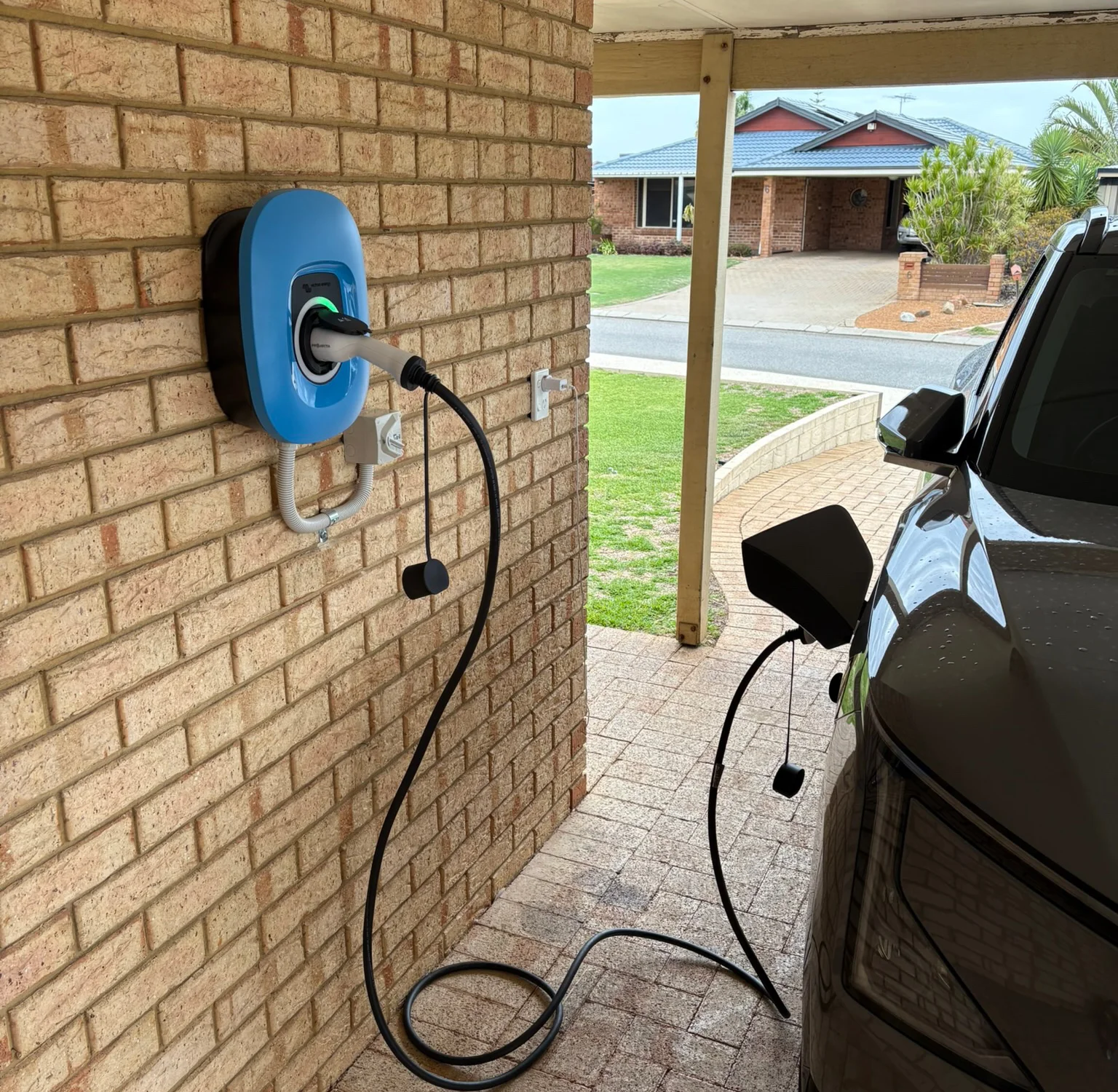 Home EV charger mounted on a brick carport wall and plugged into an electric car