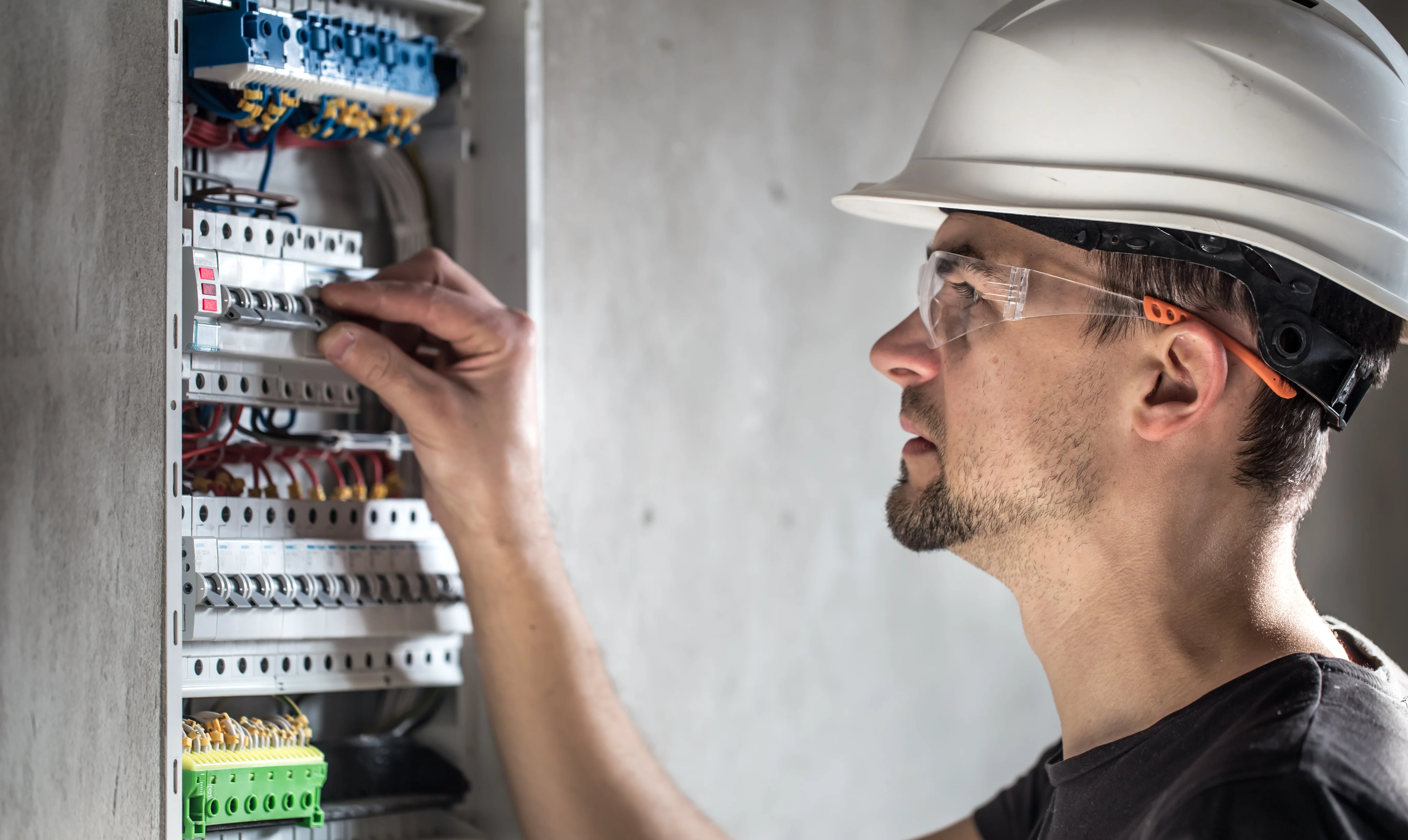 Electrician in a hard hat and safety glasses working on a switchboard