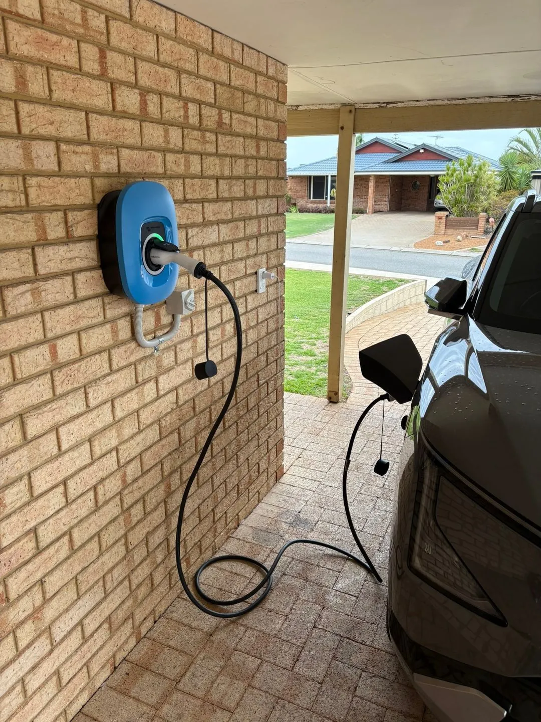 EV charger mounted on a brick wall beside a car in the driveway