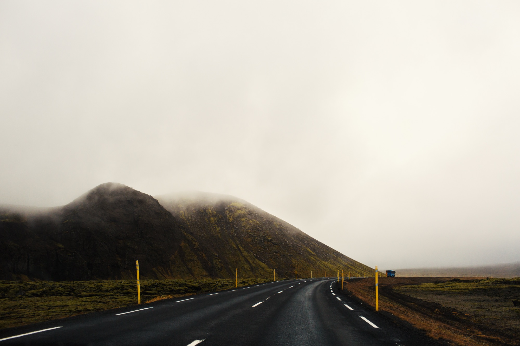 Route qui s'enfonce dans le brouillard au pied d'une colline