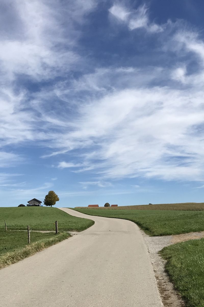Chemin entre des prairies sous un ciel de nuages légers