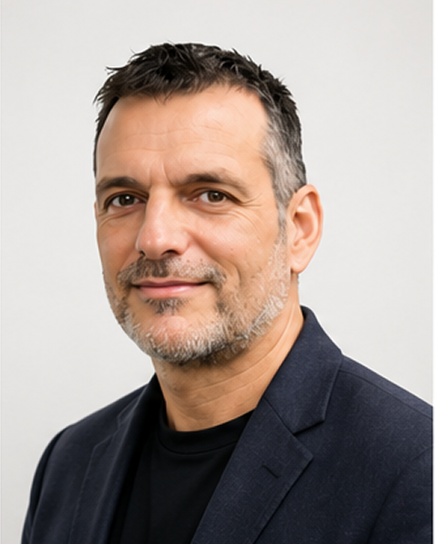 Middle-aged man with dark hair and salt-and-pepper beard wearing a navy blazer and black shirt.