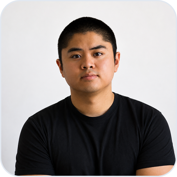 Portrait of a young man with short black hair wearing a black t-shirt, looking directly at the camera with a neutral expression on a plain white background.