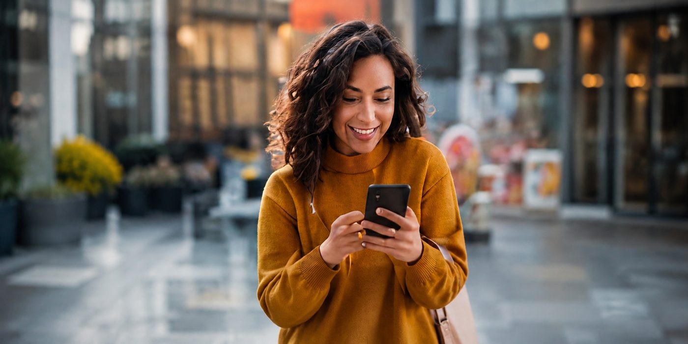 Cardholder smiling while using a mobile phone on a city street