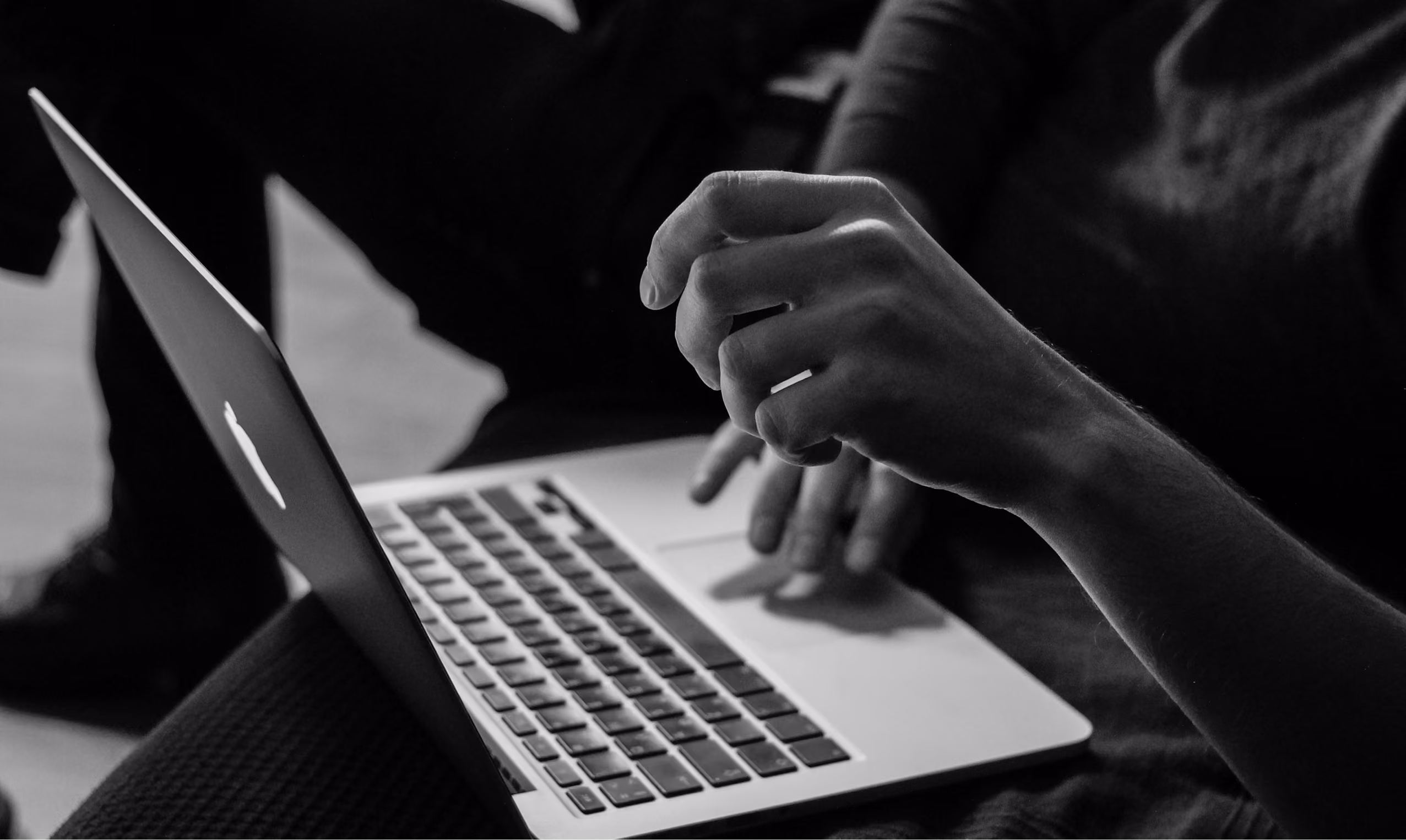 Black and white photo of a person using a laptop, with one hand poised above the keyboard and the other hand resting nearby.