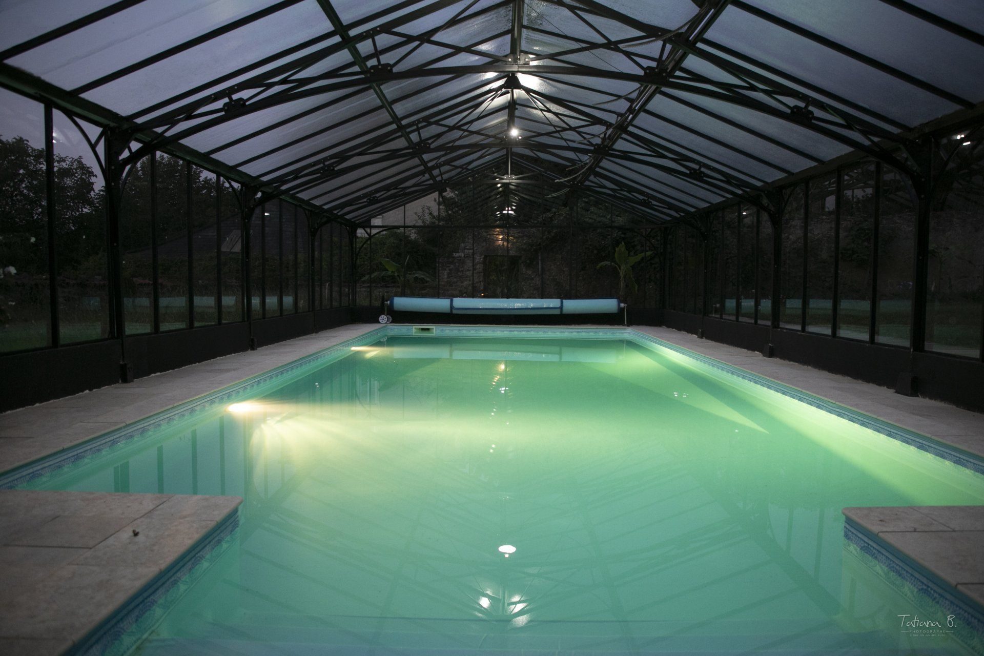 La piscine intérieure chauffée sous sa verrière, éclairée le soir