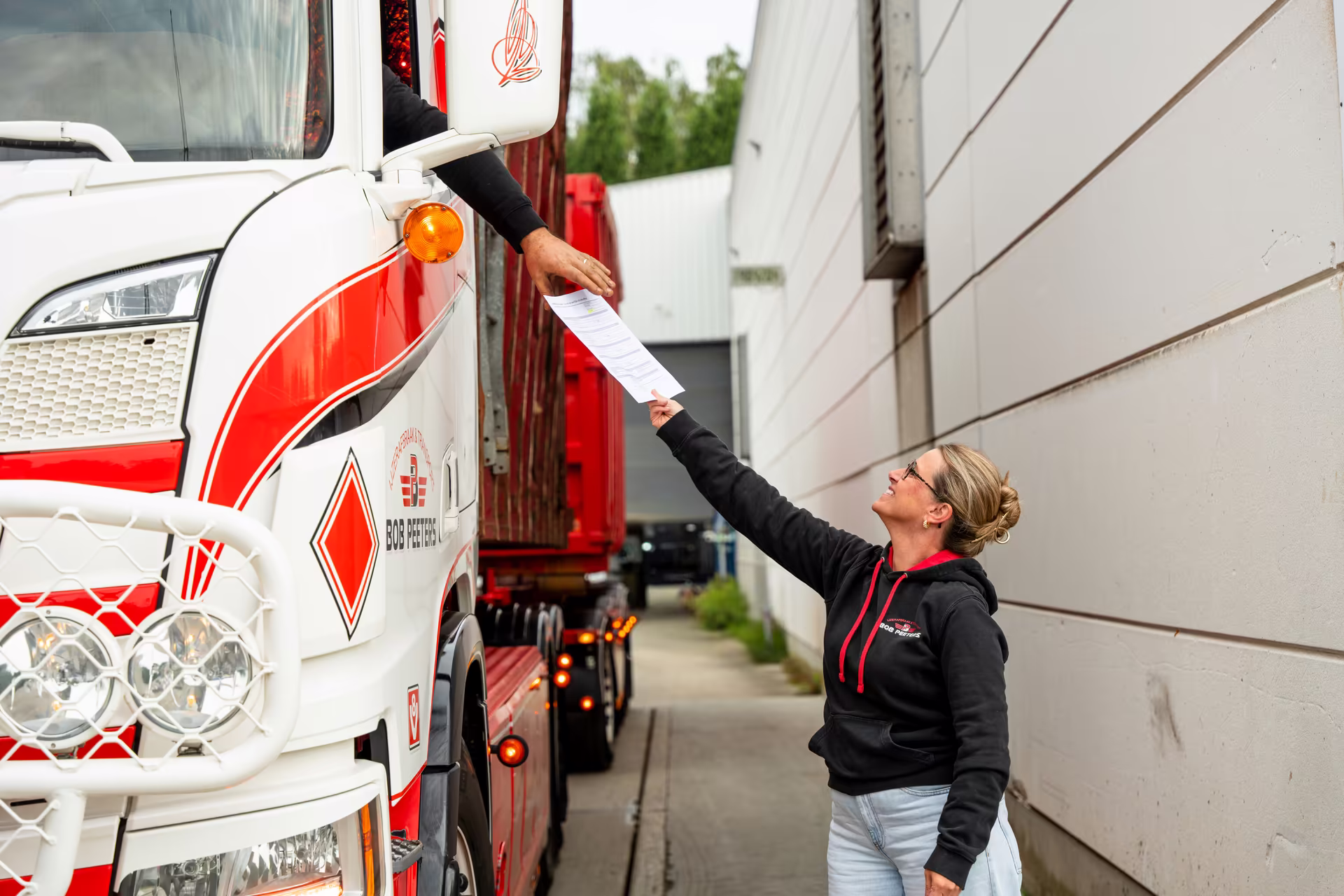 Medewerker geeft transportdocumenten aan de chauffeur van een Bob Peeters-vrachtwagen