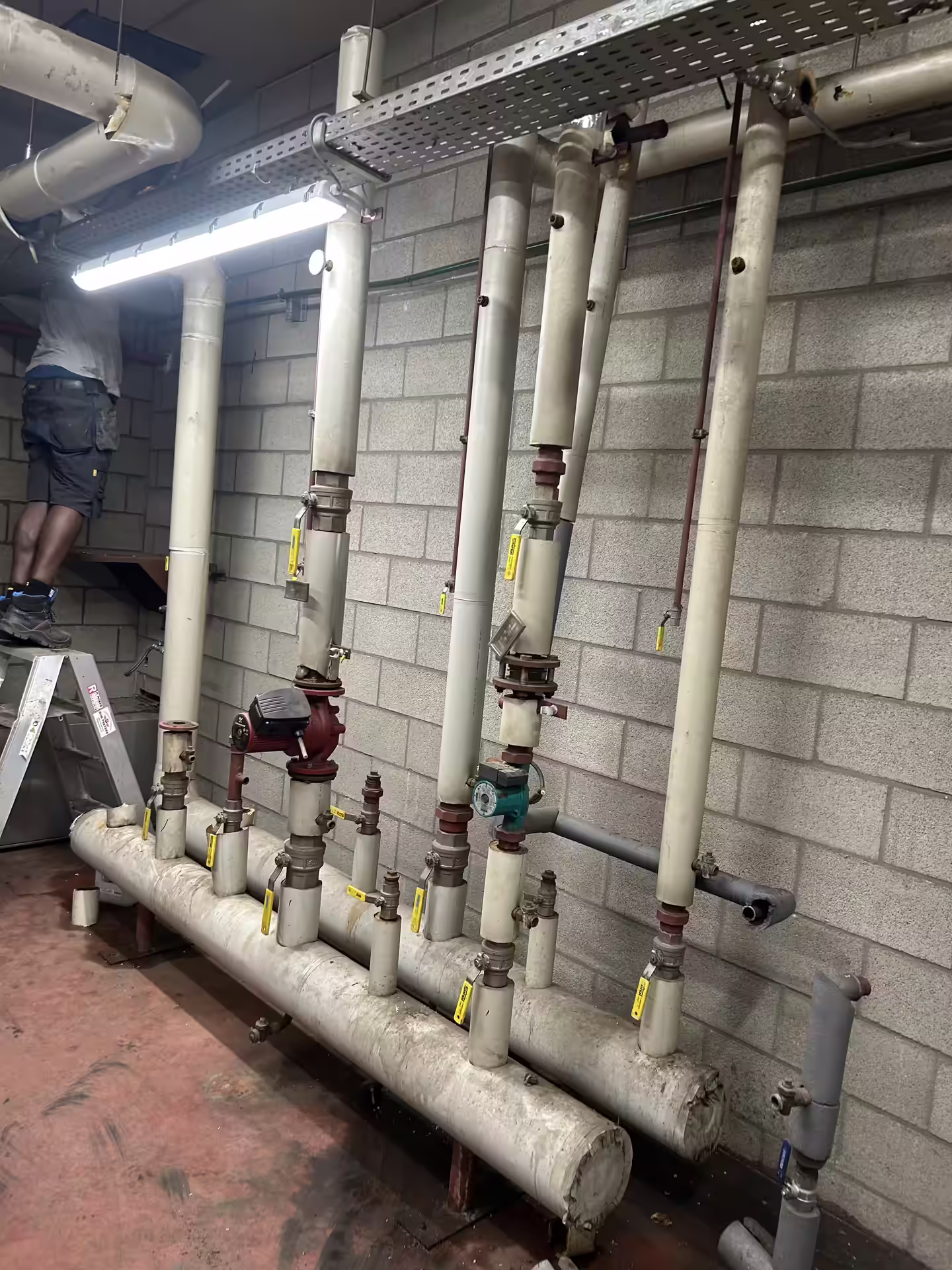 Medewerker op een ladder demonteert oude verwarmingsleidingen in een technische ruimte