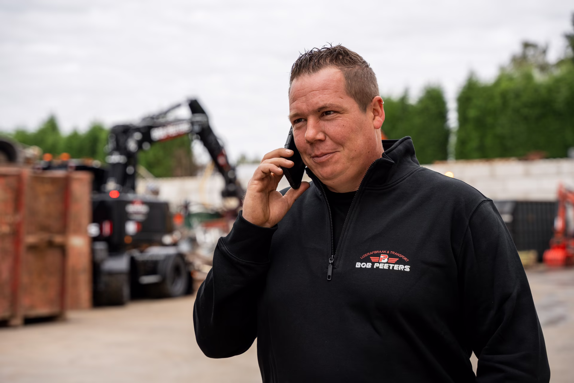 Zaakvoerder Bob Peeters aan de telefoon op de werf, met kranen en containers op de achtergrond