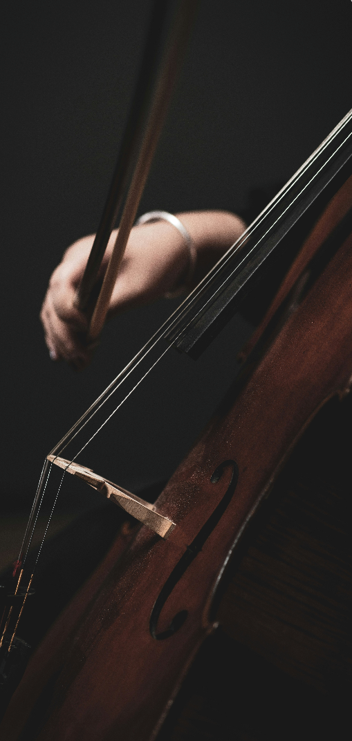 Nærbillede af en hånd, der spiller cello med bue mod mørk baggrund.