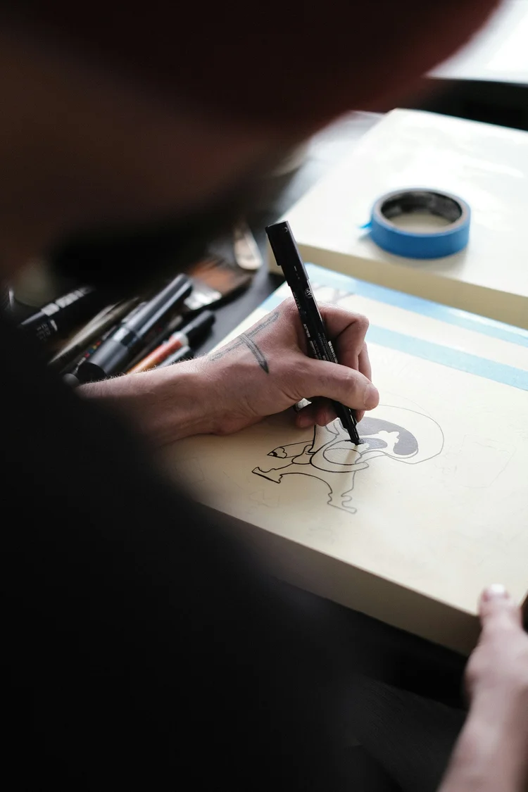 Person drawing a detailed black ink illustration on paper with a marker pen.